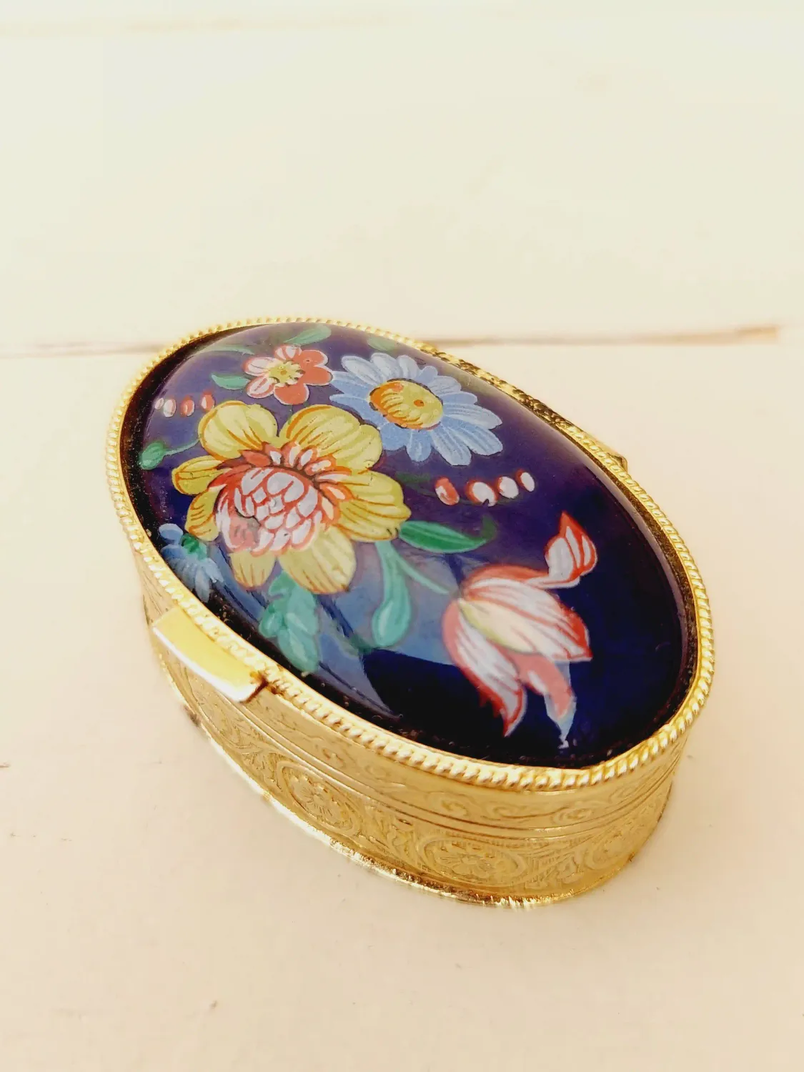 Vintage ovaal pillendoosje, blauw deksel met veldbloemen, goudkleurig doosje