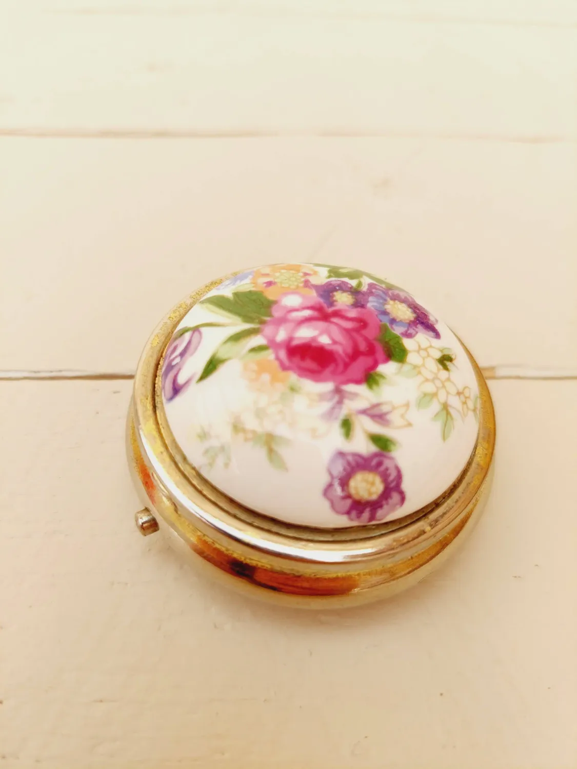 Vintage rond pillendoosje, wit deksel met kleurrijke loemen, goudkleurig doosje