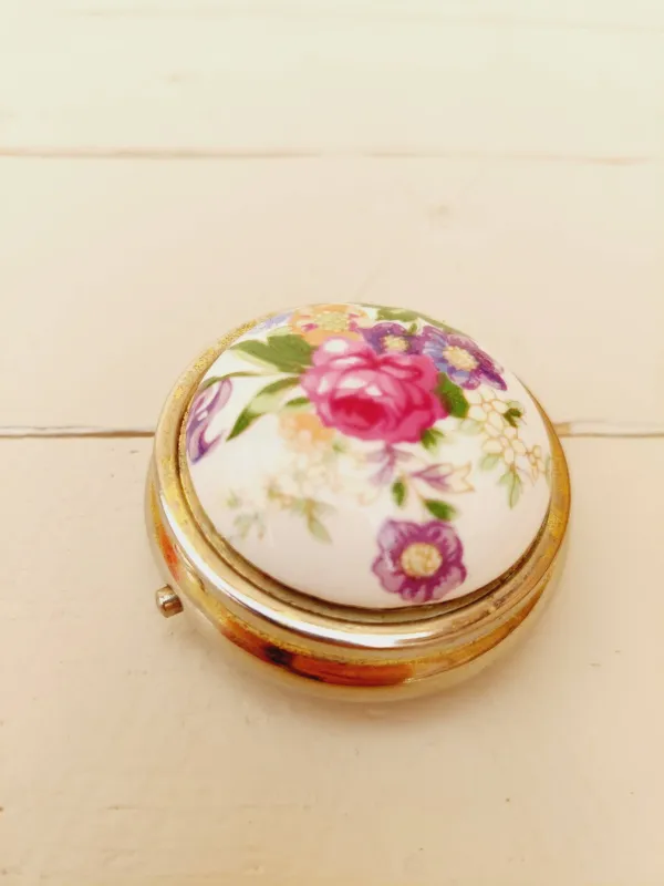 Vintage rond pillendoosje, wit deksel met kleurrijke loemen, goudkleurig doosje