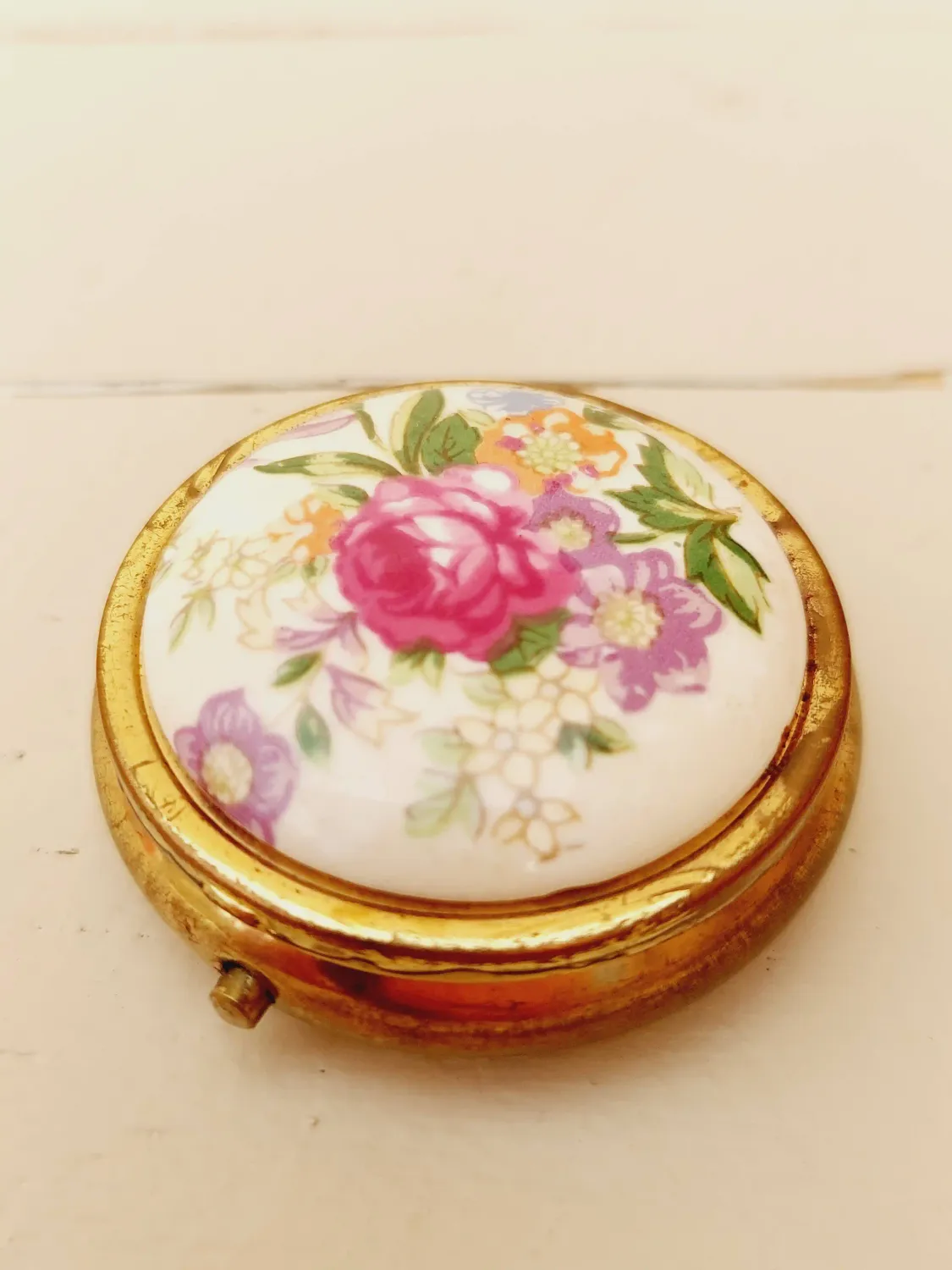 Vintage rond pillendoosje, wit deksel met kleurrijke loemen, goudkleurig doosje