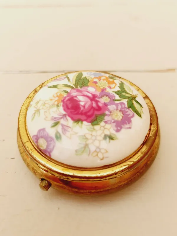 Vintage rond pillendoosje, wit deksel met kleurrijke loemen, goudkleurig doosje