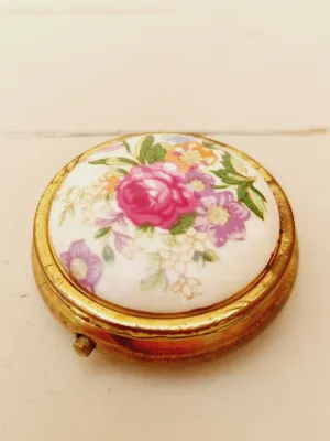 Vintage rond pillendoosje, wit deksel met kleurrijke loemen, goudkleurig doosje