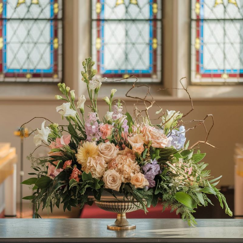 A lush orange-colored sympathy flower arrangement sits atop a table, awaiting its final display at a funeral service.