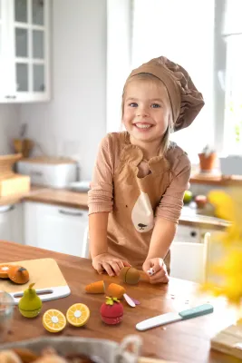 Kind speelt met houten snijfruit en groente speelgoedset van Speedy Monkey in een keuken, inclusief houten mes en snijplank.
