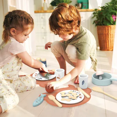 "Twee kinderen spelen samen met de houten dinerset van Speedy Monkey, gevuld met bordjes, bestek en houten etenswaren."