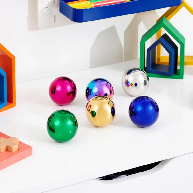 Zes reflecterende kleurrijke TickiT ballen liggen op een wit bureau in een speelhoek met felgekleurde vormen.
