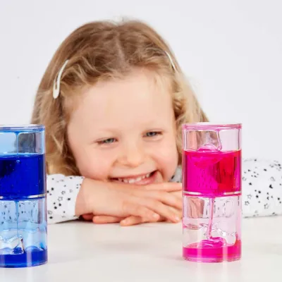 Meisje glimlacht terwijl ze naar twee kleurrijke TickiT Ooze Tubes kijkt, roze en blauw.