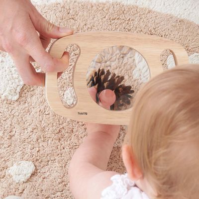 Baby bekijkt een dennenappel van dichtbij met het TickiT houten vergrootglas met 2x en 3x vergroting.