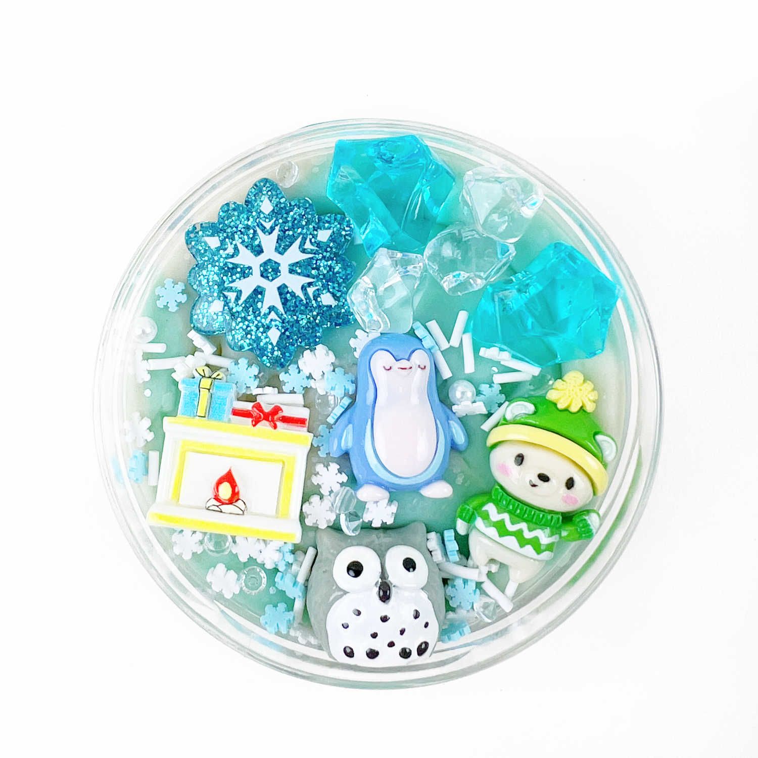 Rond bakje met winterdecoraties: glitter-sneeuwvlok, ijssteentjes, pinguïn, uil, kind in wintermuts en kleine open haard.