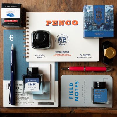 Flat lay of blue ink bottles, fountain pens, sketchbooks, and notebooks arranged on a wood background