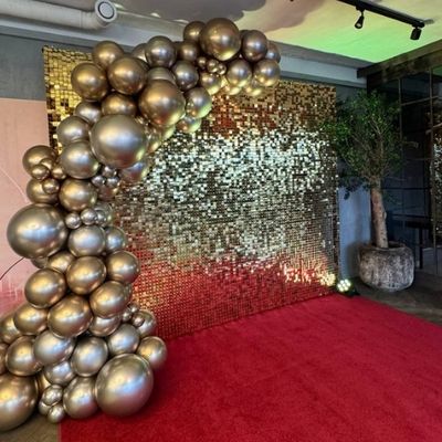 Nuotraukų siena su kilimu ir balionais
Elegantiškas dekoras su auksine nuotraukų siena, balionų girlianda ir minkštu kilimu, suteikiantis šventei išskirtinį stilių. Elegant event decor set with a golden photo wall, balloon garland, and rug