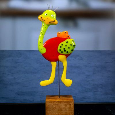 Glasfigur, struds, orange krop, gult hoved og vinge, rød hale, grønne ben, går mod venstre på træfod