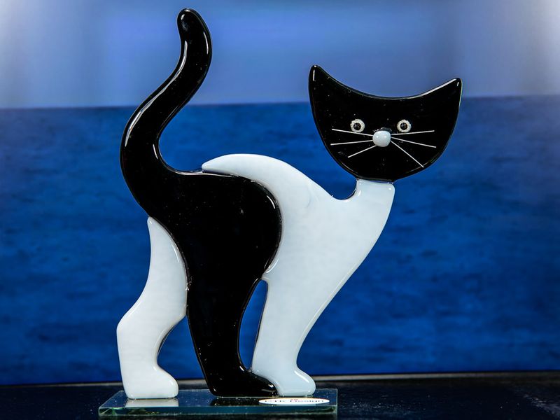 Glasfigur, sort hvid, med sort hoved, går mod højre, på glasfod