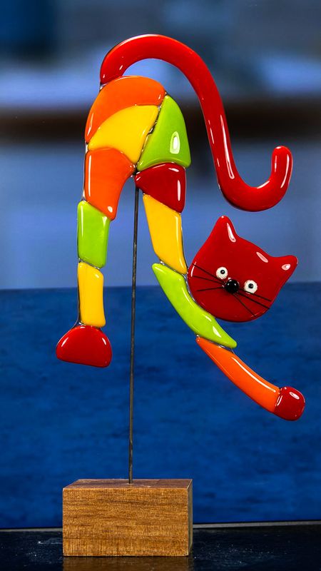 Glasfigur, kat, mange farvet, med rødt hoved, vender mod højre, på træfod