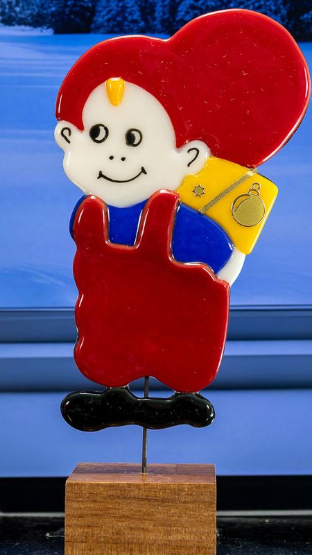 Glasfigur Nissedreng med blå bluse, gul pakke på ryggen, ser på venstre, på træfod