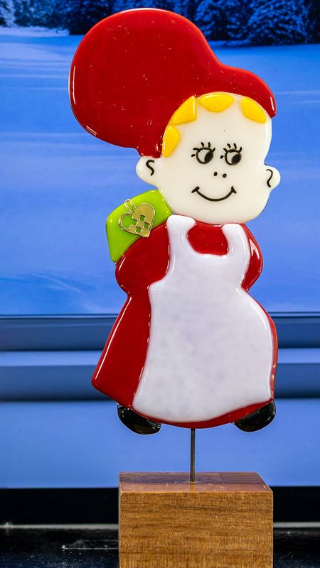 Glasfigur Nissepige, ser mod højre, med grøn pakke på ryggen, på træfod