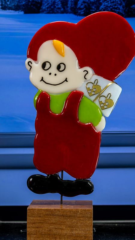 Glasfigur Nissedreng med grøn bluse,hvid pakke på ryggen, ser mod venstre, på træfod