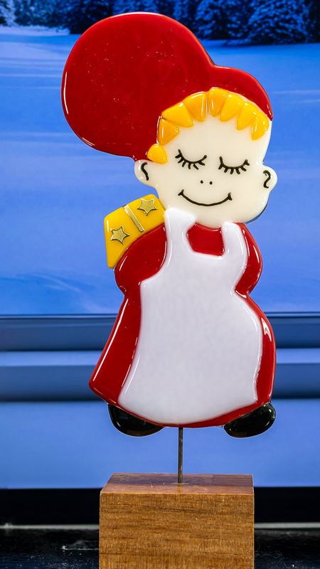 Glasfigur Nissepige, vender mod højre, med gul pakke på ryggen, på træfod