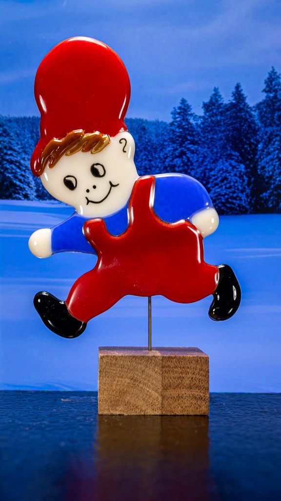 Glasfigur Nissedreng med blå bluse, løber mod venstre, på træfod Glasfigur Nissedreng med blå bluse, løber mod venstre, på træfod