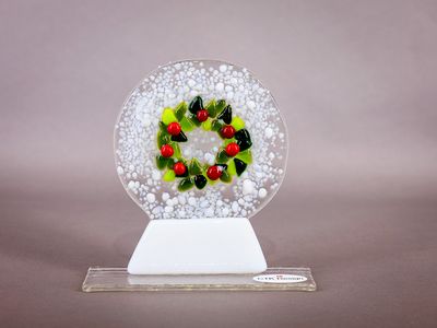 Glasfigur, snekugle, dørkrans, på glasfod Grøn og rød julekrans i rund klar glasskive med hvid sne og hvid fod.