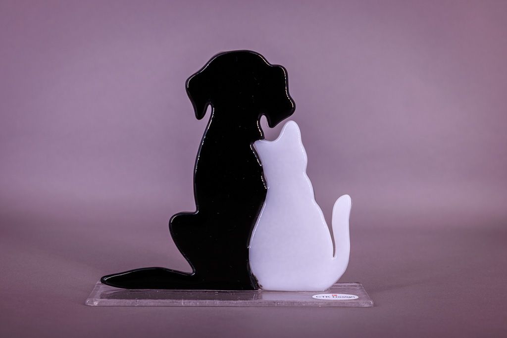 Håndlavet glasfigur med sort hund og hvid kat siddende tæt sammen på en klar glasfod.