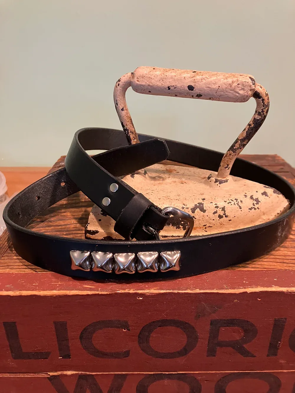 Two 1 inch belts displayed on rustic wood - one black leather with antique brass hardware, the other oxblood with silver