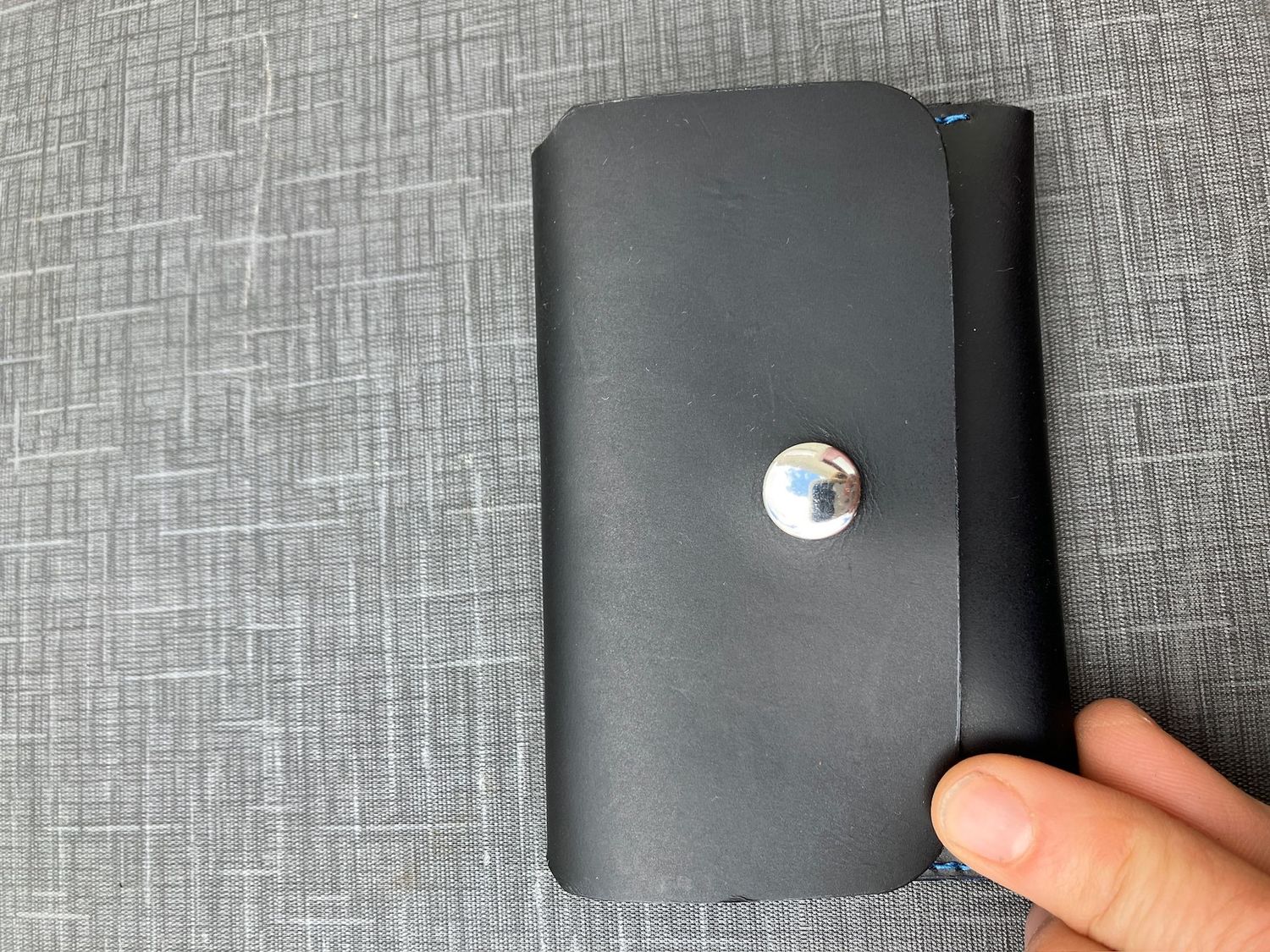 A hand holding the Small snap wallet in black with silver snap
