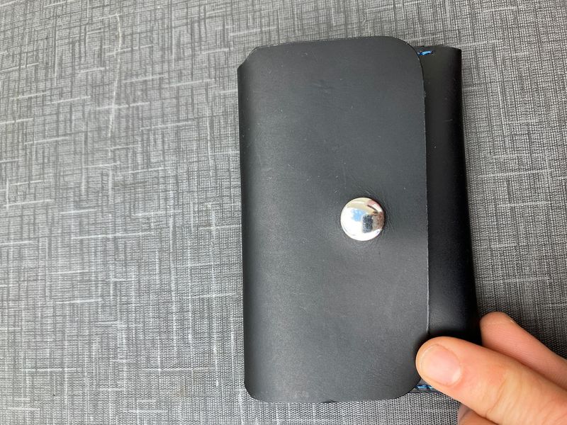 A hand holding the Small snap wallet in black with silver snap