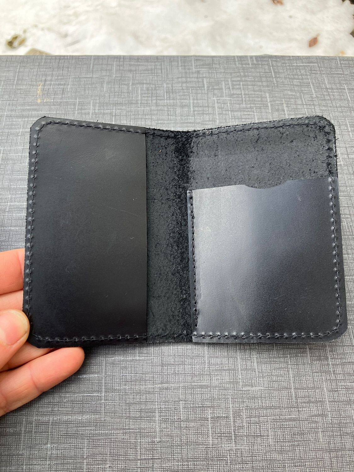 A hand holding open the small two-fold wallet in black