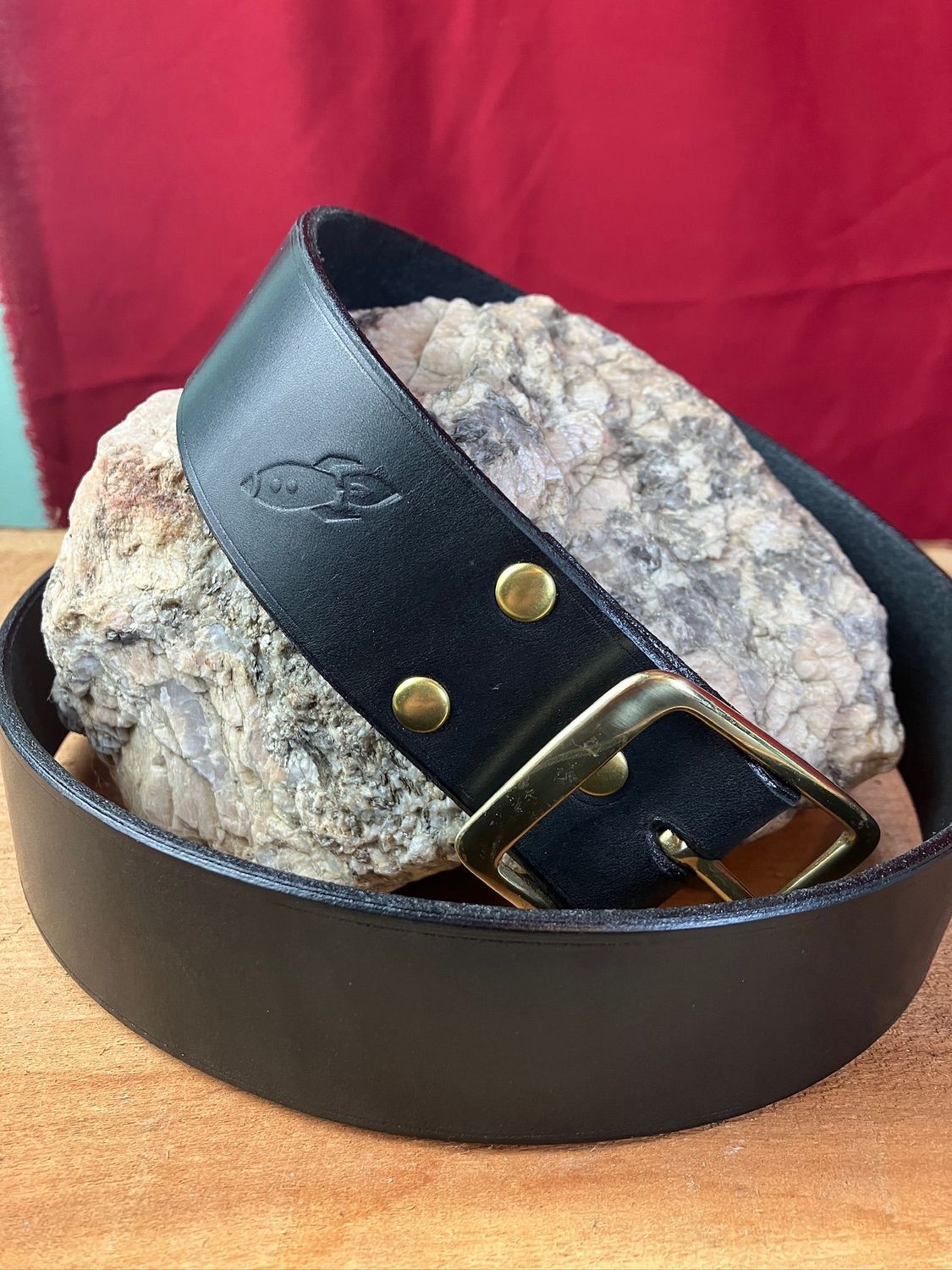 A beautiful black leather belt wrapped around a piece of granite, this one featuring a brass buckle and rivets.