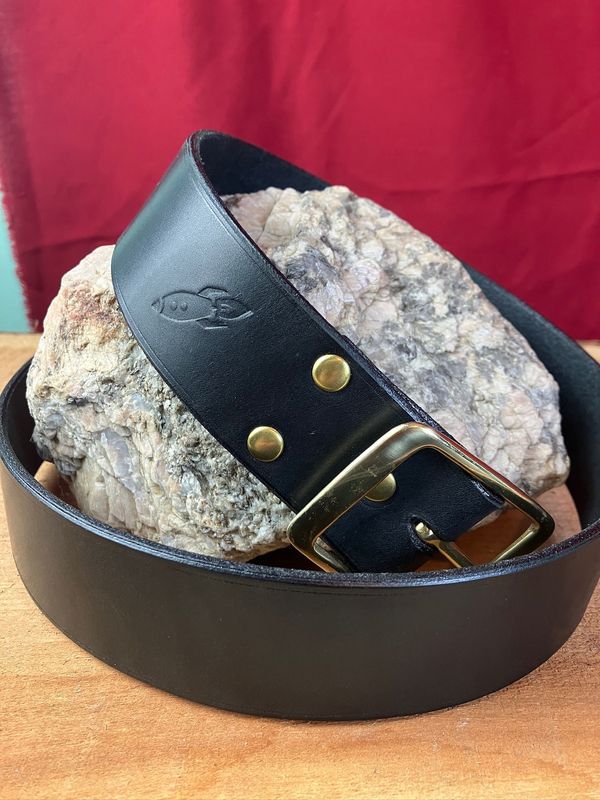A beautiful black leather belt wrapped around a piece of granite, this one featuring a brass buckle and rivets.