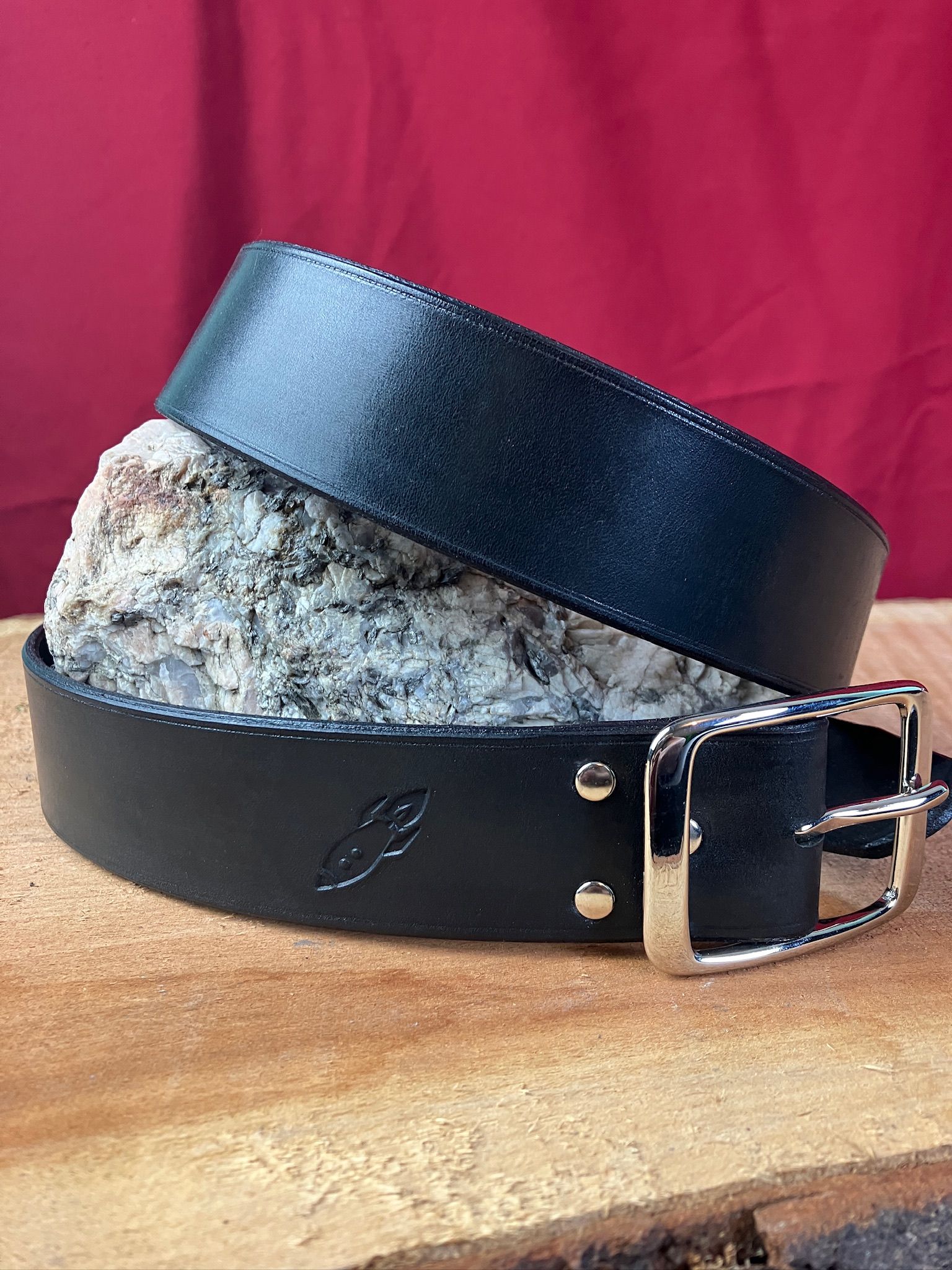 A beautiful black leather belt wrapped around a piece of granite, this one featuring a brass buckle and rivets.