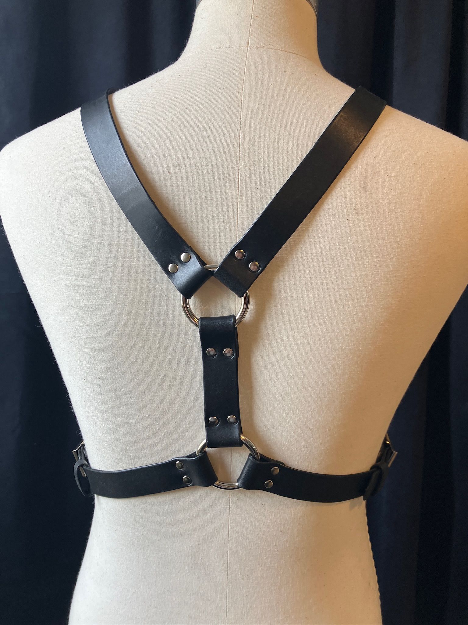 An off-white mannequin displaying the Front Andros chest harness in black. It looks like a Y on the body with a belt
