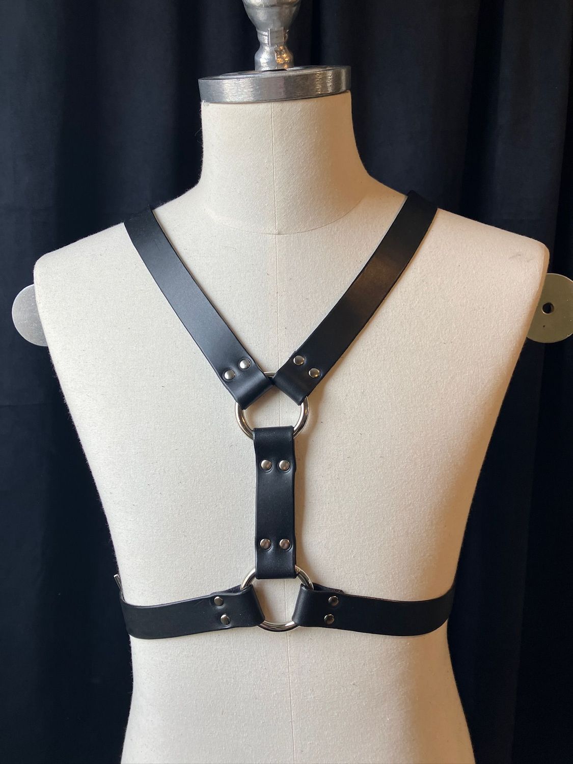 An off-white mannequin displaying the Front Andros chest harness in black. It looks like a Y on the body with a belt 