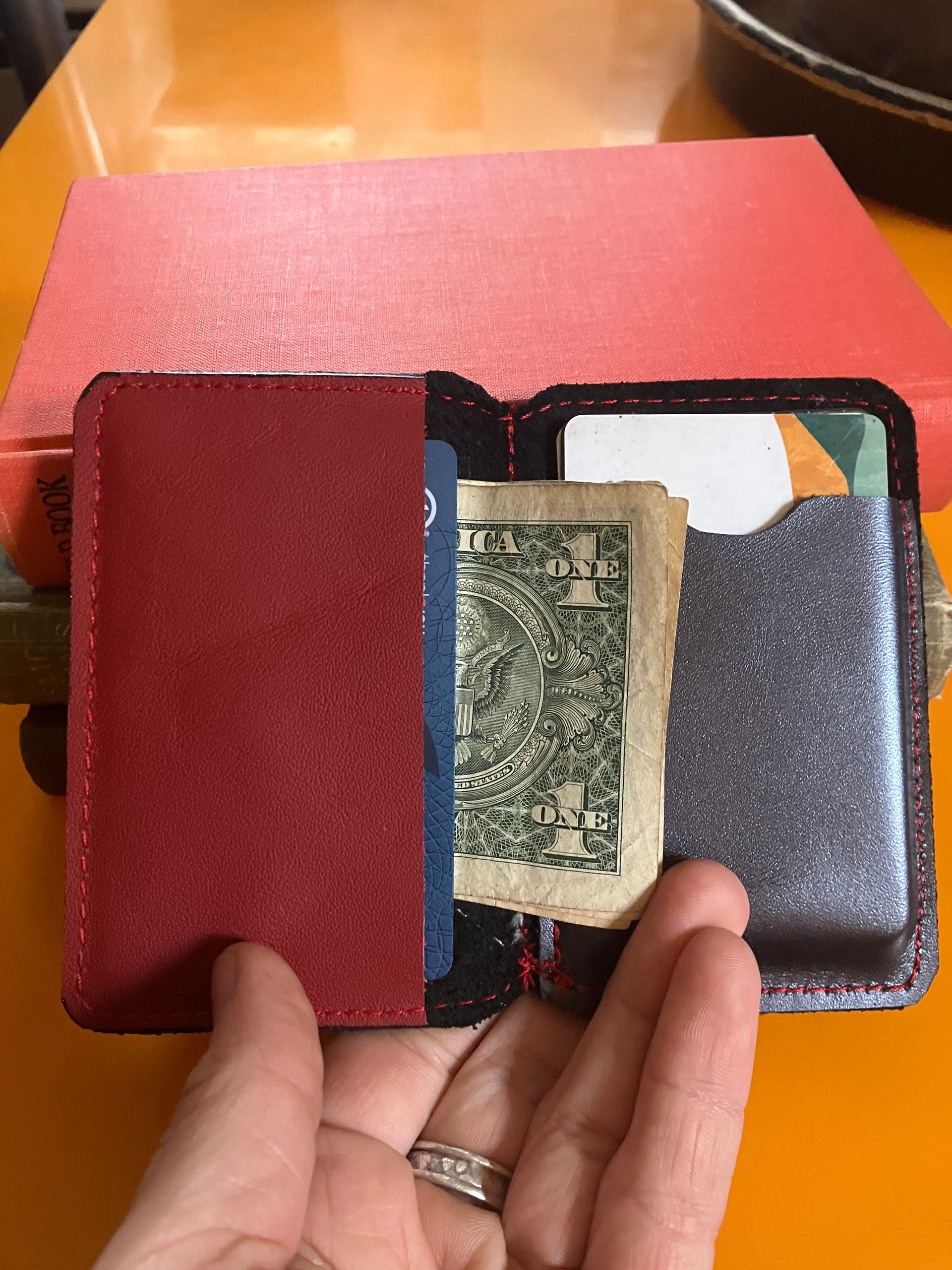 A hand holding the Small Twin Peaks wallet front facing with background of old books