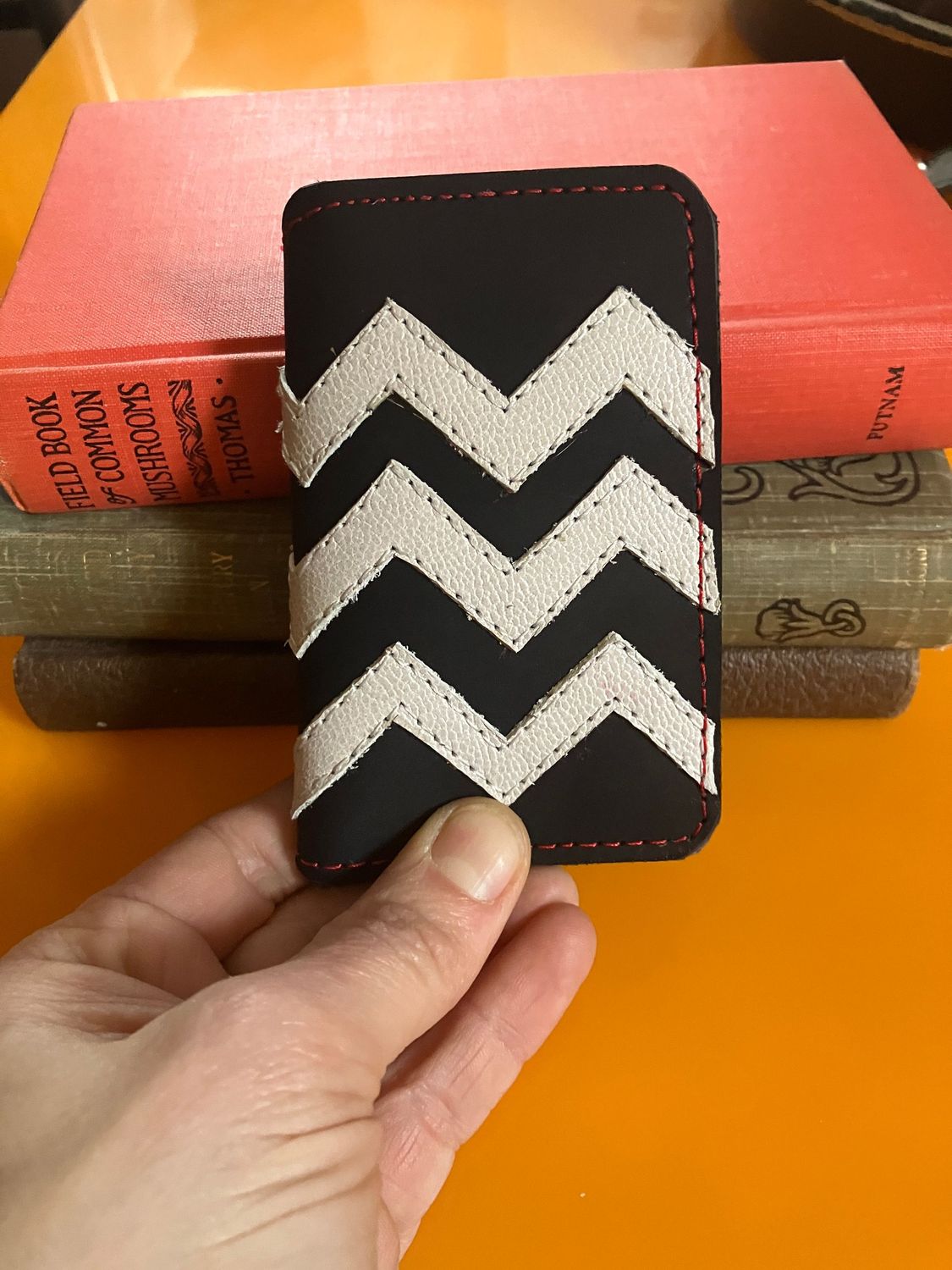 A hand holding the Small Twin Peaks wallet front facing with background of old books