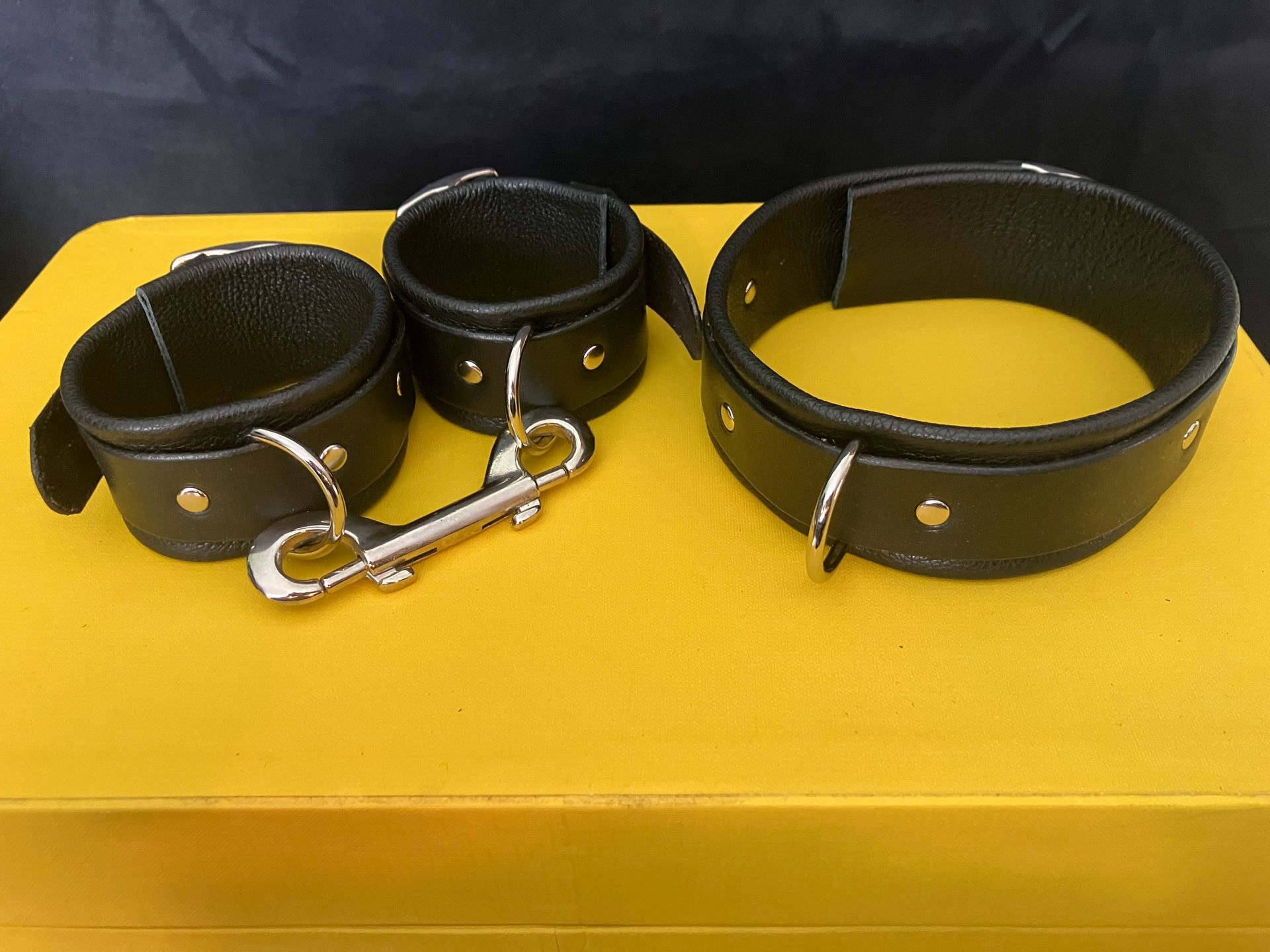 An image of the bondage cuffs and collar in black with silver hardware - and double clip addition for the cuff joining.