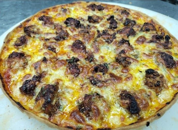 A delicious Manchurian Pizza topped with a fusion of flavors, featuring crispy vegetable Manchurian balls, melted mozzarella cheese, and a spicy Manchurian sauce. The pizza is adorned with vibrant bell peppers, onions, and a sprinkle of fresh coriander, all sitting on a perfectly baked crust. Served hot on a wooden board, it's a unique blend of Indian and Italian cuisine that's sure to tantalize your taste buds.