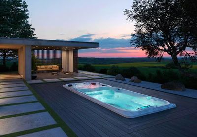 Jacuzzi® PowerActive™ J-19 Bi-zone spa de nage encastré dans un terrace en bois noir avec lumière allumé