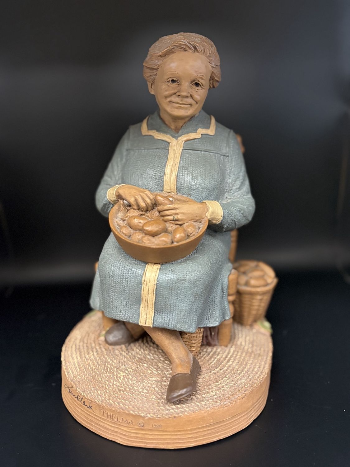 Sculpted Figure. USA. Tom Clark. Thelma. Woman in blue dress sitting in a chair holding a bowl of potatoes. 1987. 10&quot;H