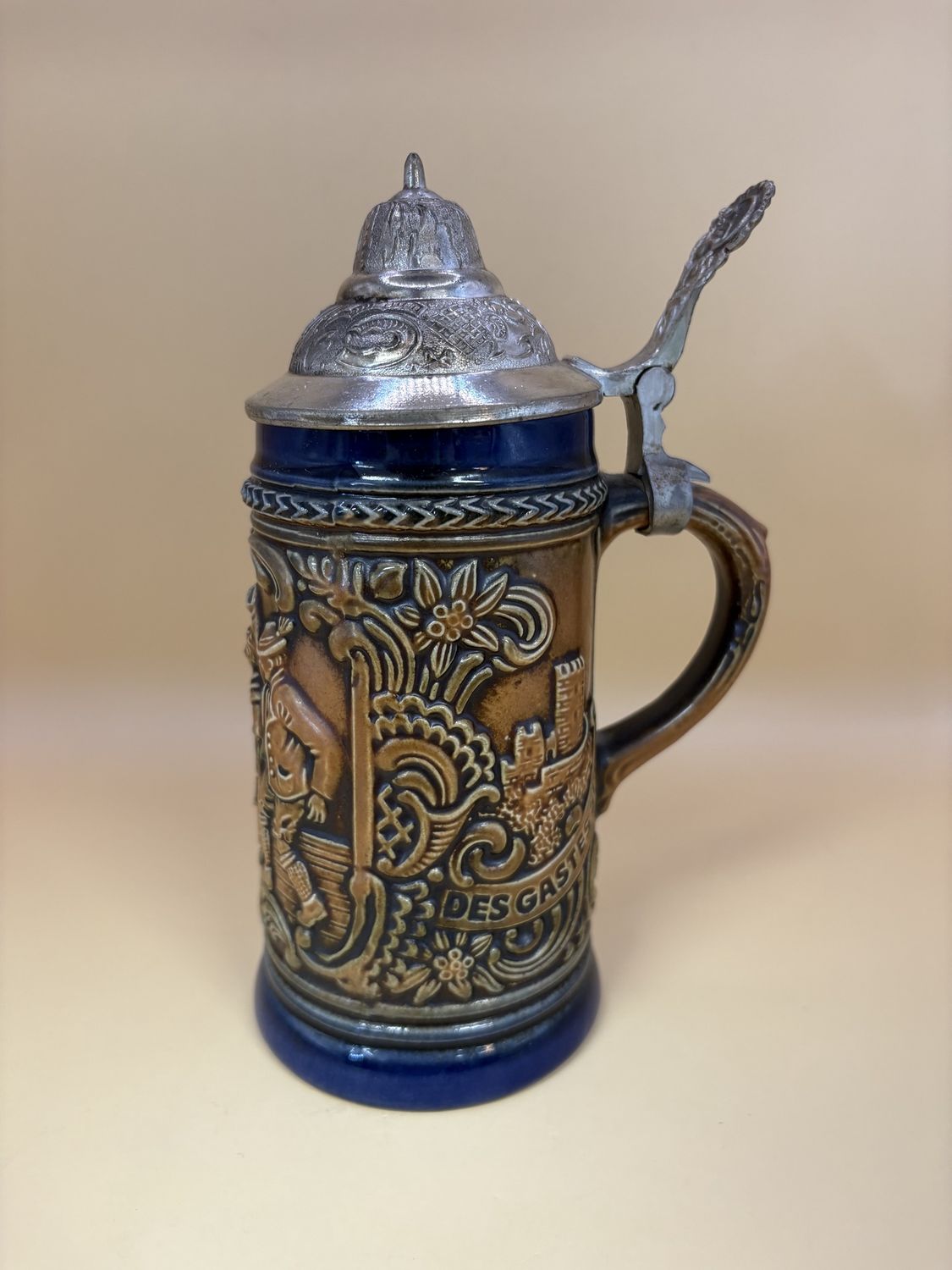 Stein. Germany. Two Men &amp; Woman Dancing w/ Beer. Edelweiss Design w/ Text &quot;Ein Volles Glas Des Gastes Spab&quot;. Brown w/ Dark Blue Outline. Pewter Lid. 7.25&quot;H