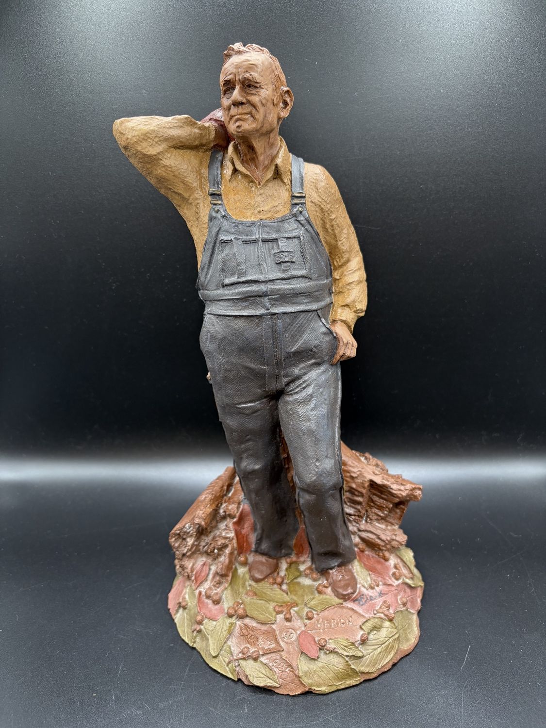 Sculpted Figure. USA. Tom Clark. &quot;Marion the Farmer.&quot; Man Leaning Back w/ Logs Around Feet. 1985. Signed. 12&quot;H