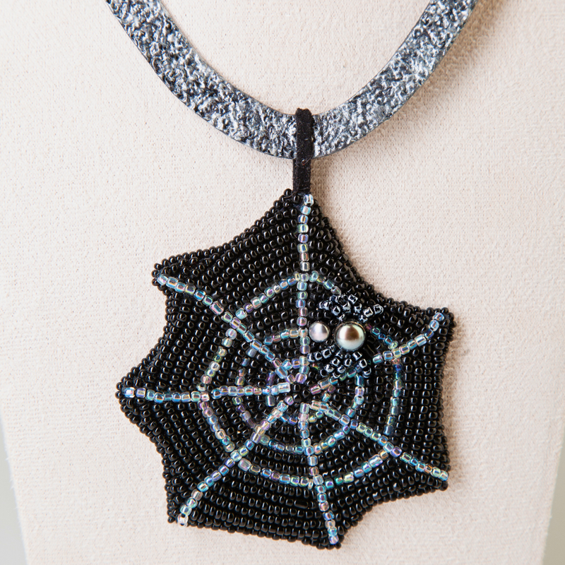 Tooled leather Gothic necklace imitating a hammered silver with a pendant featuring a pearl spider sitting on a bead embroidered spider web