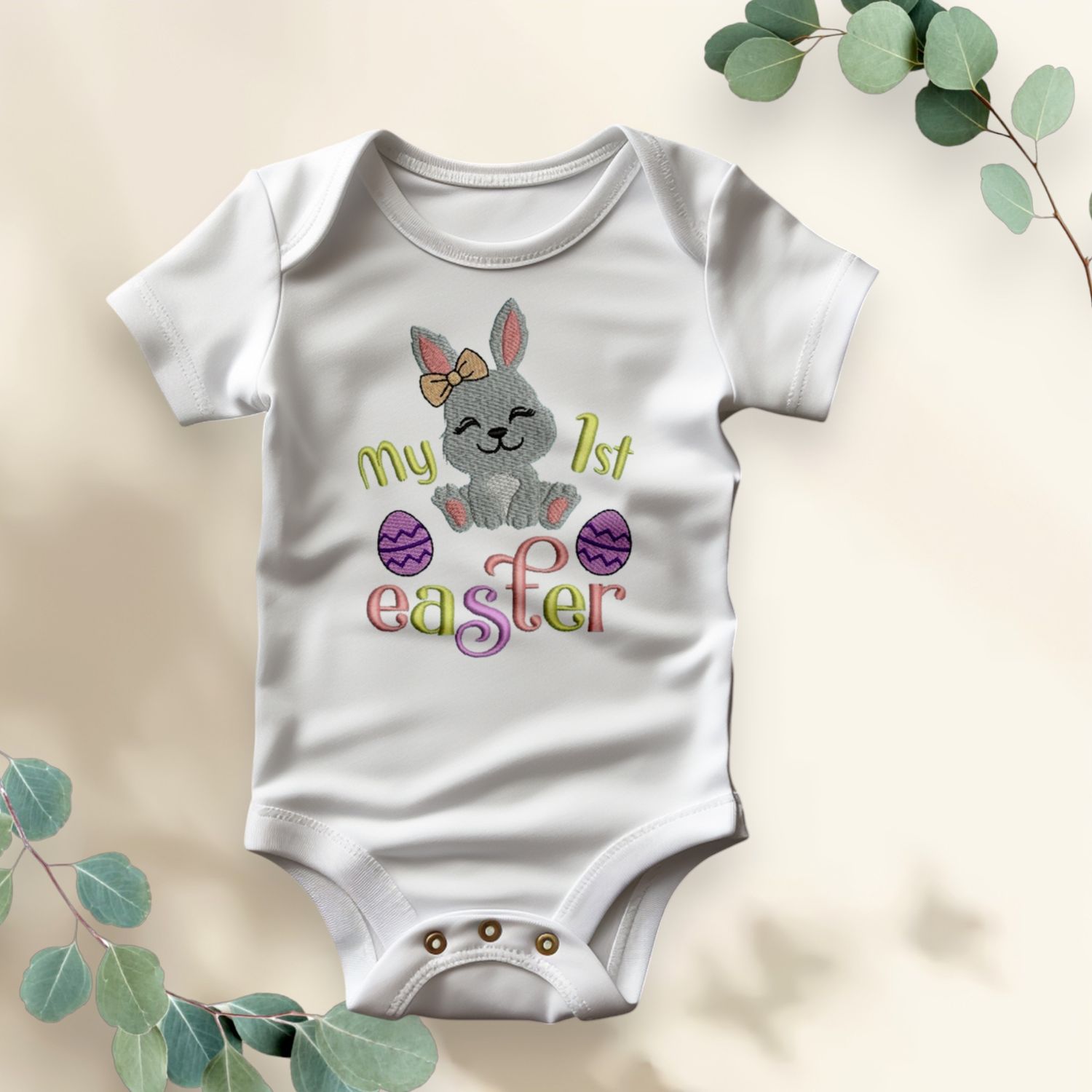 Wit babyrompertje met opdruk van een paashaas, paaseieren en tekst &quot;My 1st Easter&quot; in vrolijke kleuren.
