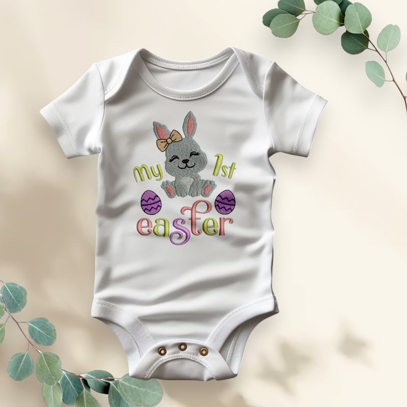 Wit babyrompertje met opdruk van een paashaas, paaseieren en tekst &quot;My 1st Easter&quot; in vrolijke kleuren.