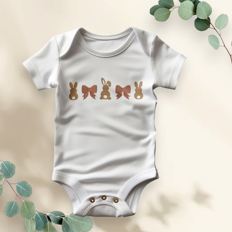 Witte babyromper met gouden konijntjes en strikken, ideaal als stijlvolle Paasoutfit of uniek kraamcadeau.