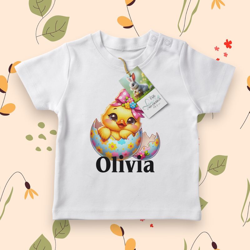 Wit baby T-shirt met een schattig geel kuikentje, versierd met een roze strik en een vrolijk paasei.