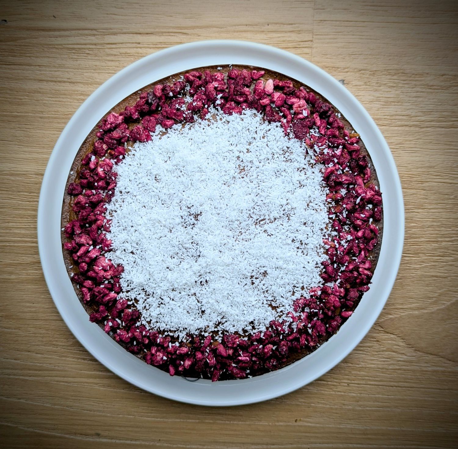 Flan Pie: Glutenvrij en lactosevrij taartje met amandelmeel, speculaaskruiden, gevriesdroogde frambozen en kokosschaafsel. Een zoete traktatie van Angies Atelier.
