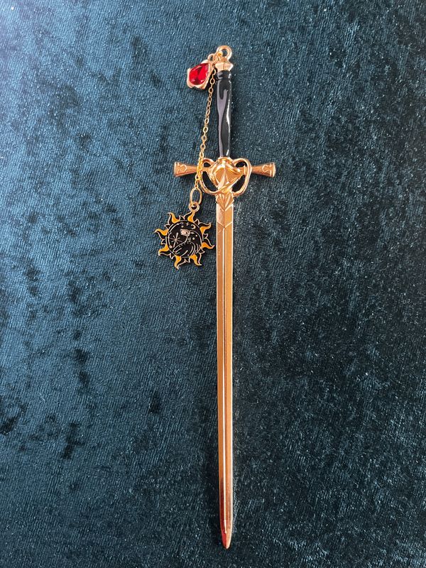 Lesezeichen "Schwert" in Gold-Optik mit schwarzem Griff, rotem Stein,  Kettchen und Anhänger "Sonne & Rabe"