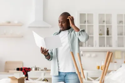 A man is standing in a kitchen looking at a piece of paper.